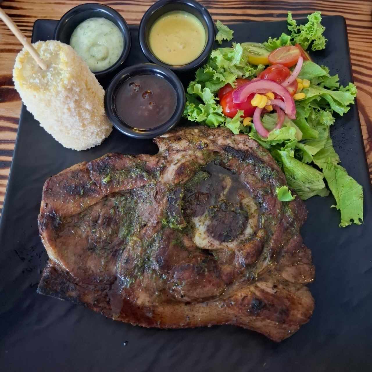 Chuleta de cerdo acompañada con elote en queso parmesano y ensalada