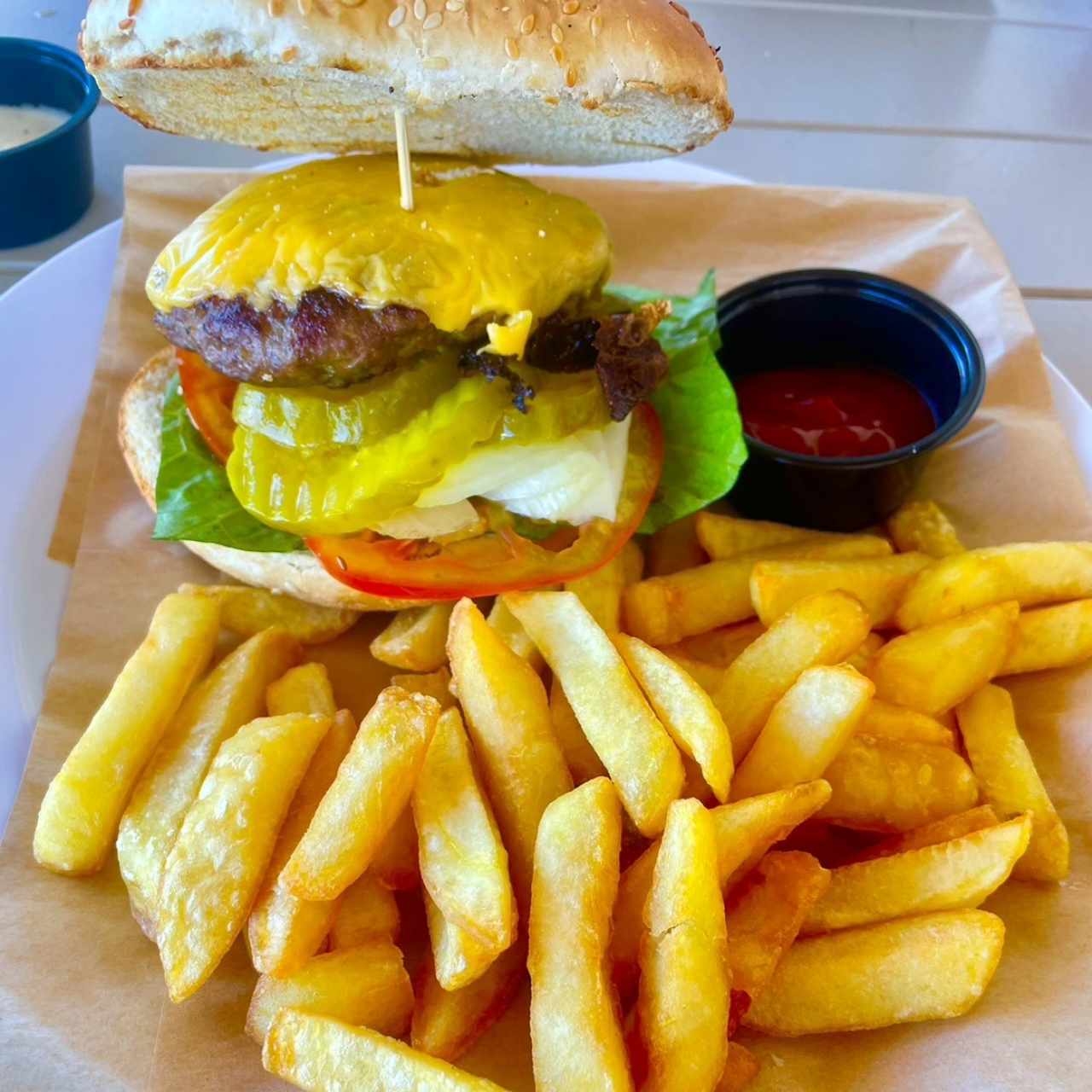 HAMBURGUESA BLUE BEACH (Carne a la Parrilla, Queso Fundido, Bacón y Nuestros Ingredientes Clásicos:  Lechuga, Tomate, Cebolla v Pepinillos) con Papas Fritas