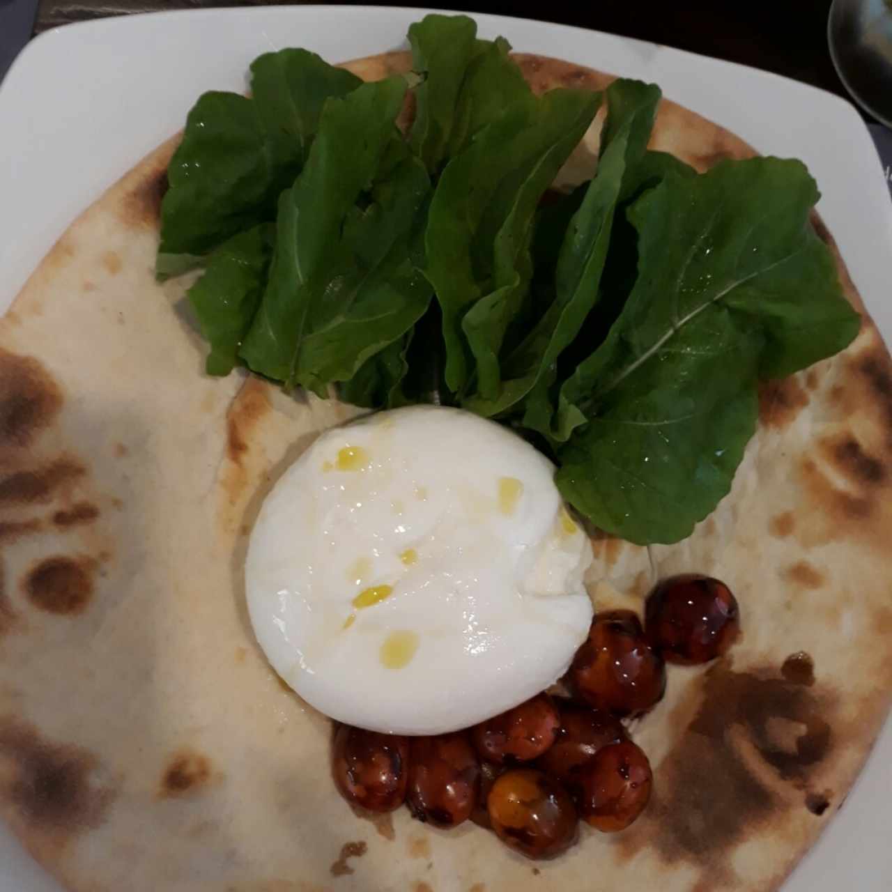 Burrata bufalina sobre una cama de focaccia, tomatitos borrifado con aceite extra virgen y aceite balsámico