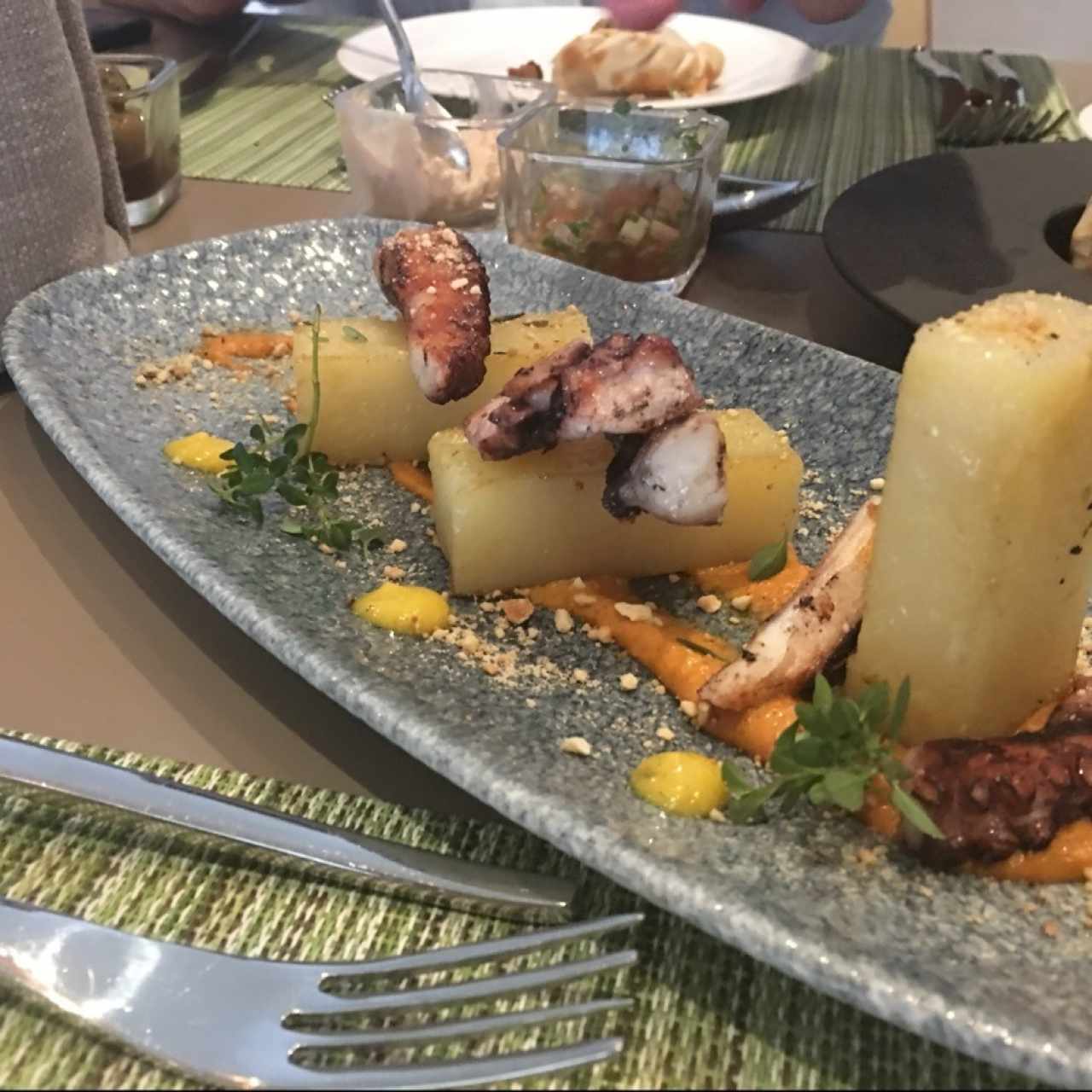 PULPO MARINADO en aceite de cítricos, papas bouchon, crema de pimientos y pepitas de marañón, aderezo de curry.