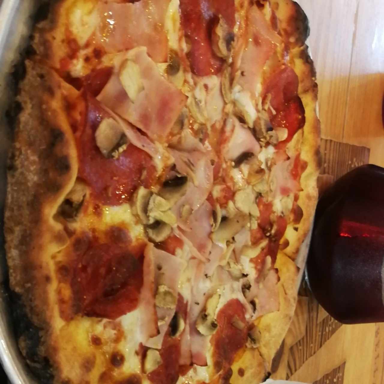 Pizza de masa gluten free con peperoni, jamón y hongos. Al fondo la sangría