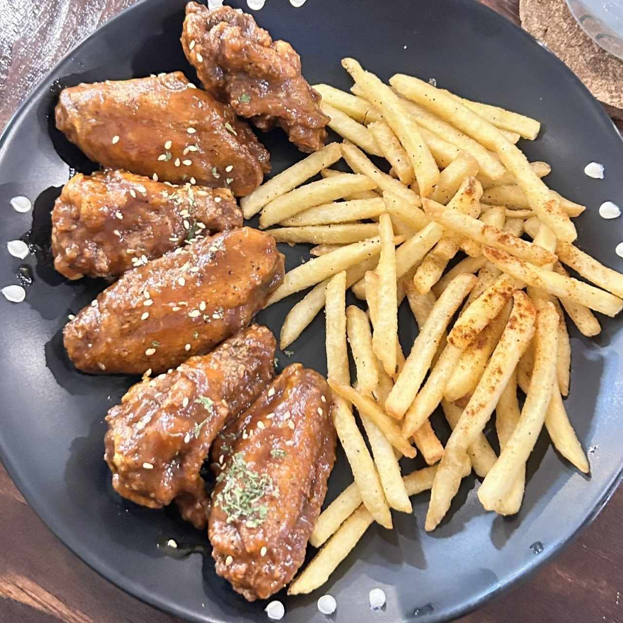 Wings Tropical Flow Alitas de pollo bañadas en salsa BBQ mango-coco (salsa hecha en casa) con Flow ahumado y coronadas con ajonjolí acompañadas con papas fritas. Nivel de picante bajo.