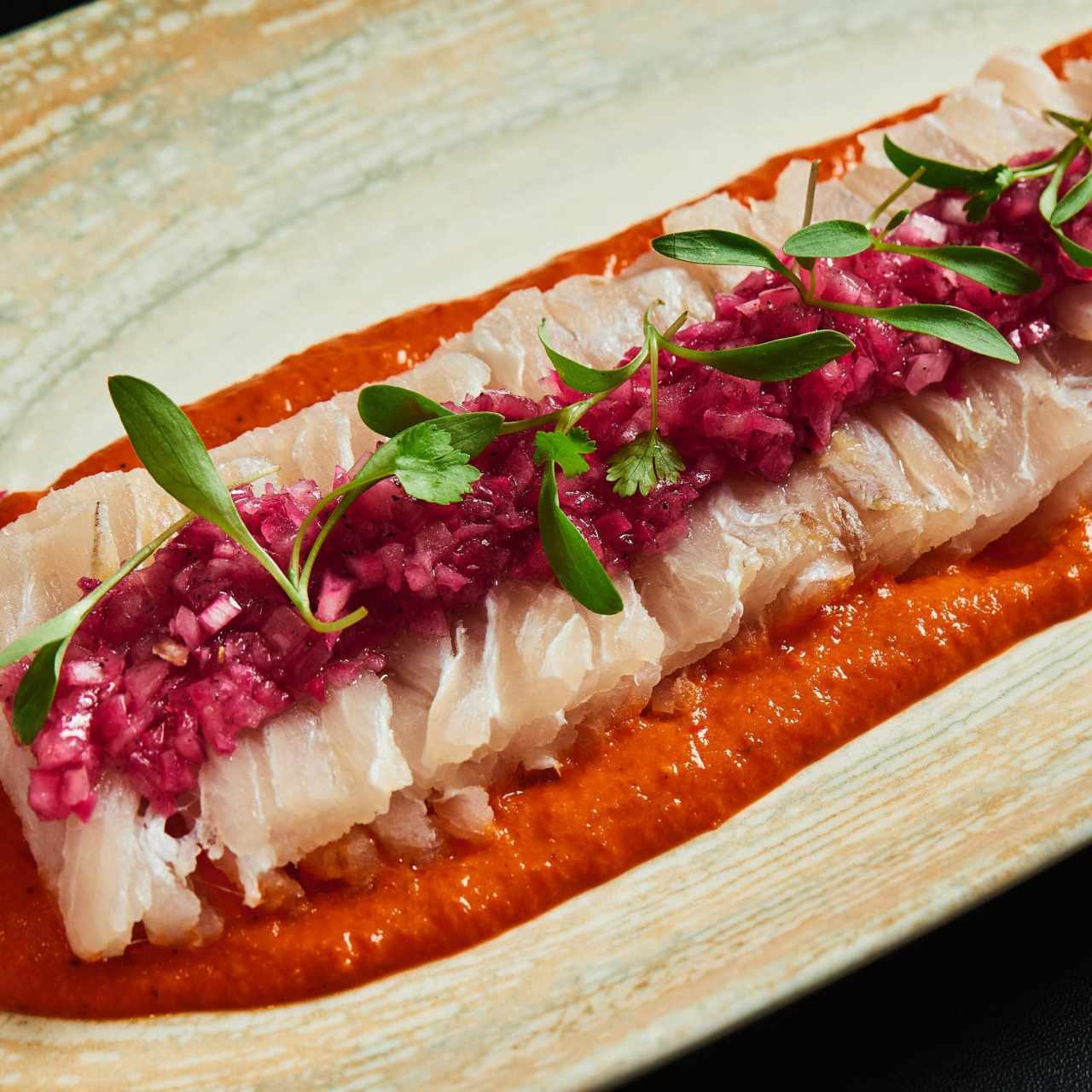 Tiradito de róbalo sobre crema de ají trompito ahumado, brotes de cilantro y relish de cebolla morada