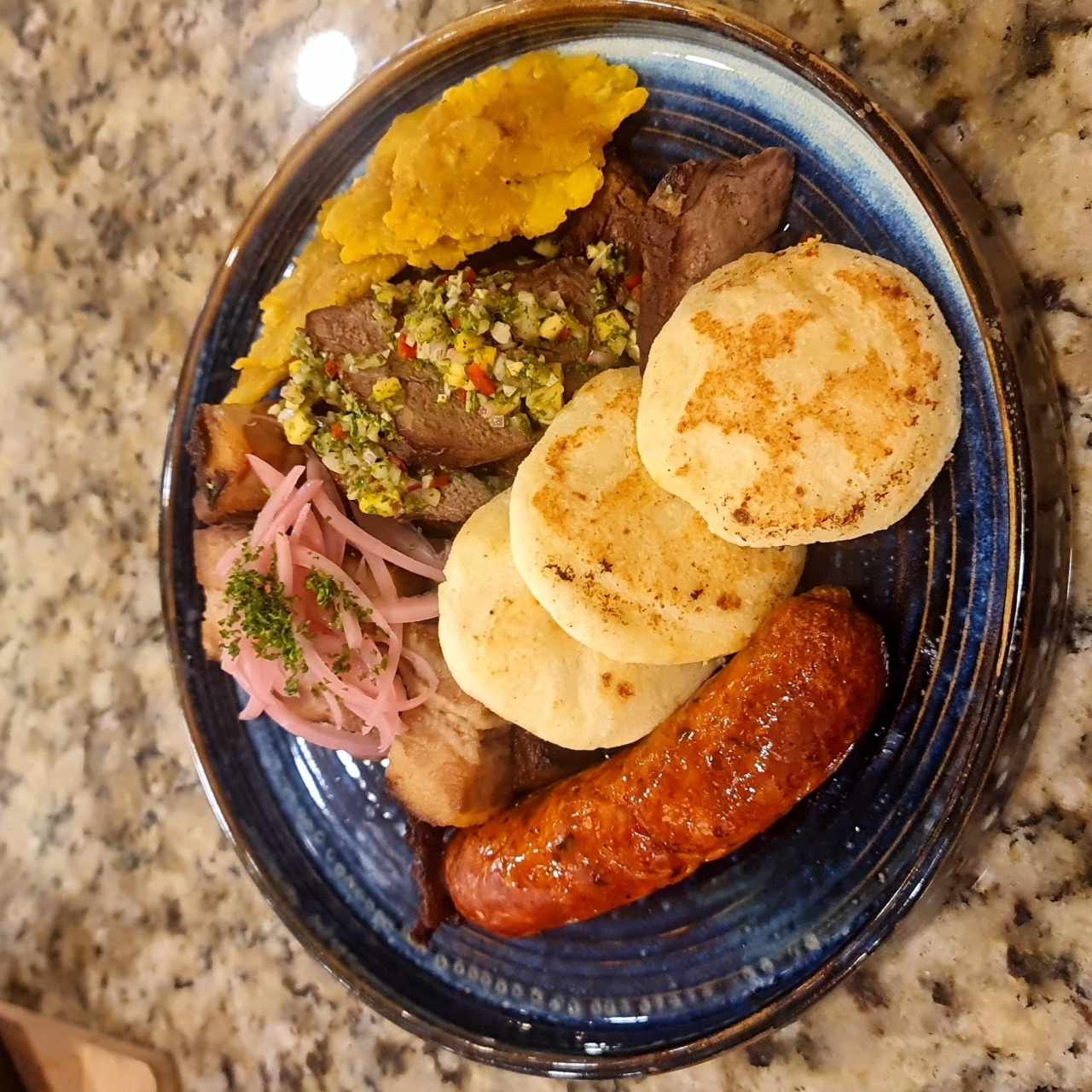 Picada típica ideal para dos con trozos de chicharrón de cerdo ahumado coronado con cebolla encurtida, carne de res y chorizo tableño, acompañada de tortillas de maíz con queso y patacones con salsa fresca de culantro