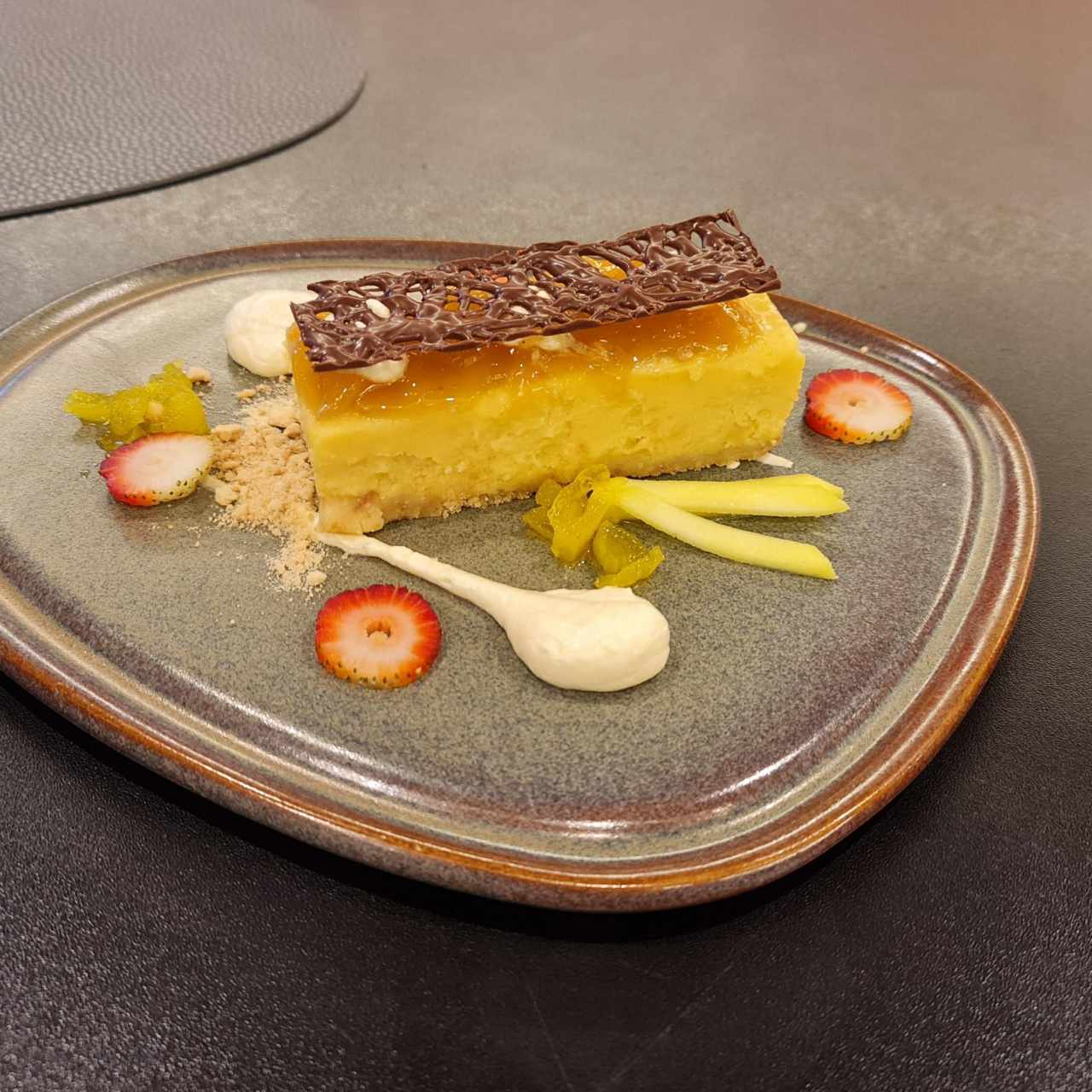 Cremoso pastel de queso bañado en salsa de mango tropical sobre crumble de vainilla con hierba buena fresca